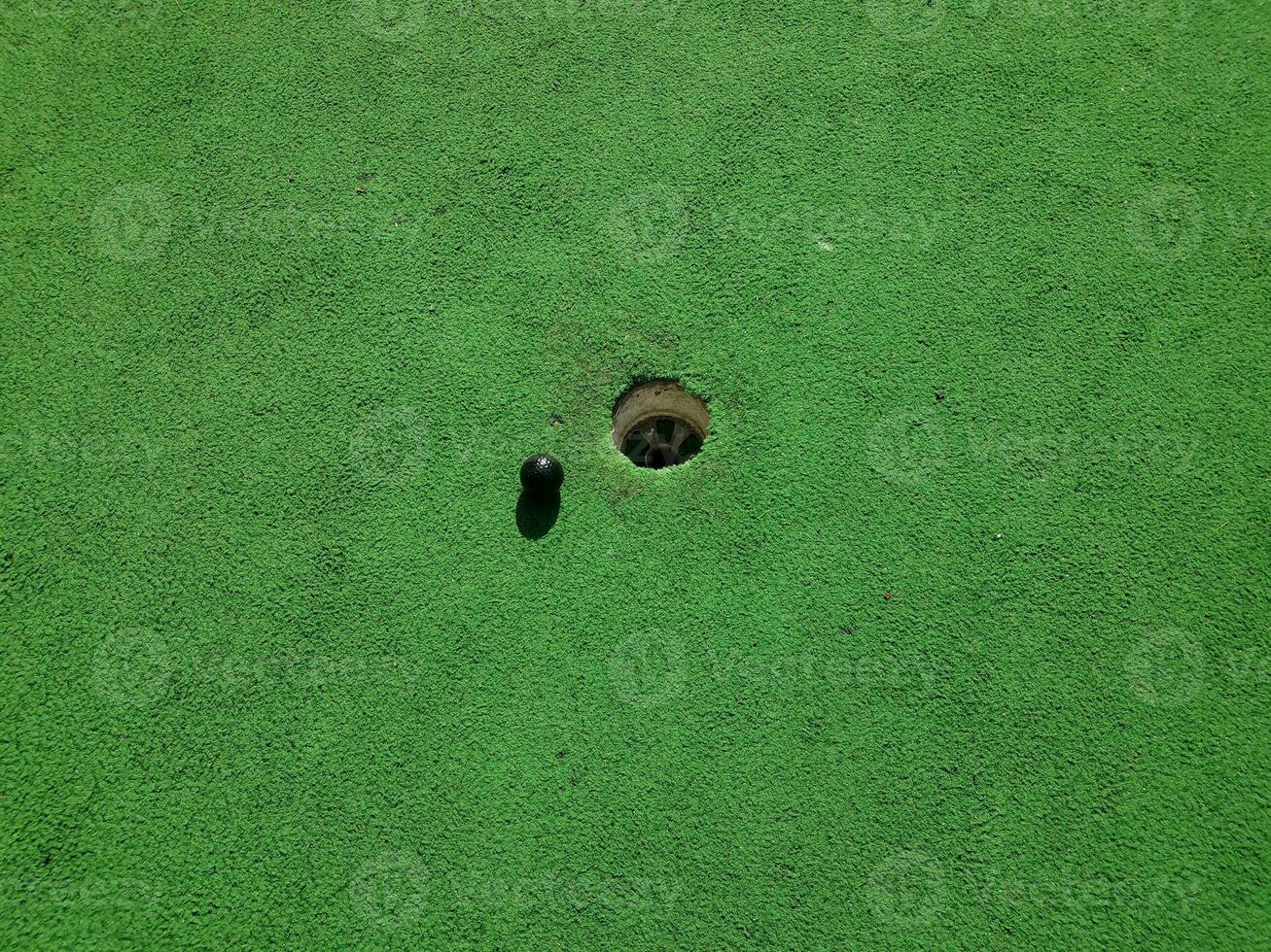 hole op midgetgolfbaan met groen kunstgras en zwarte bal foto