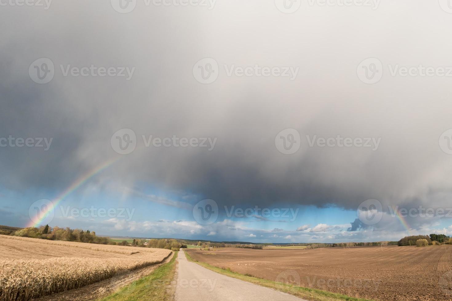 panorama van het veld langs de weg met een regenboog en stormachtige lucht foto