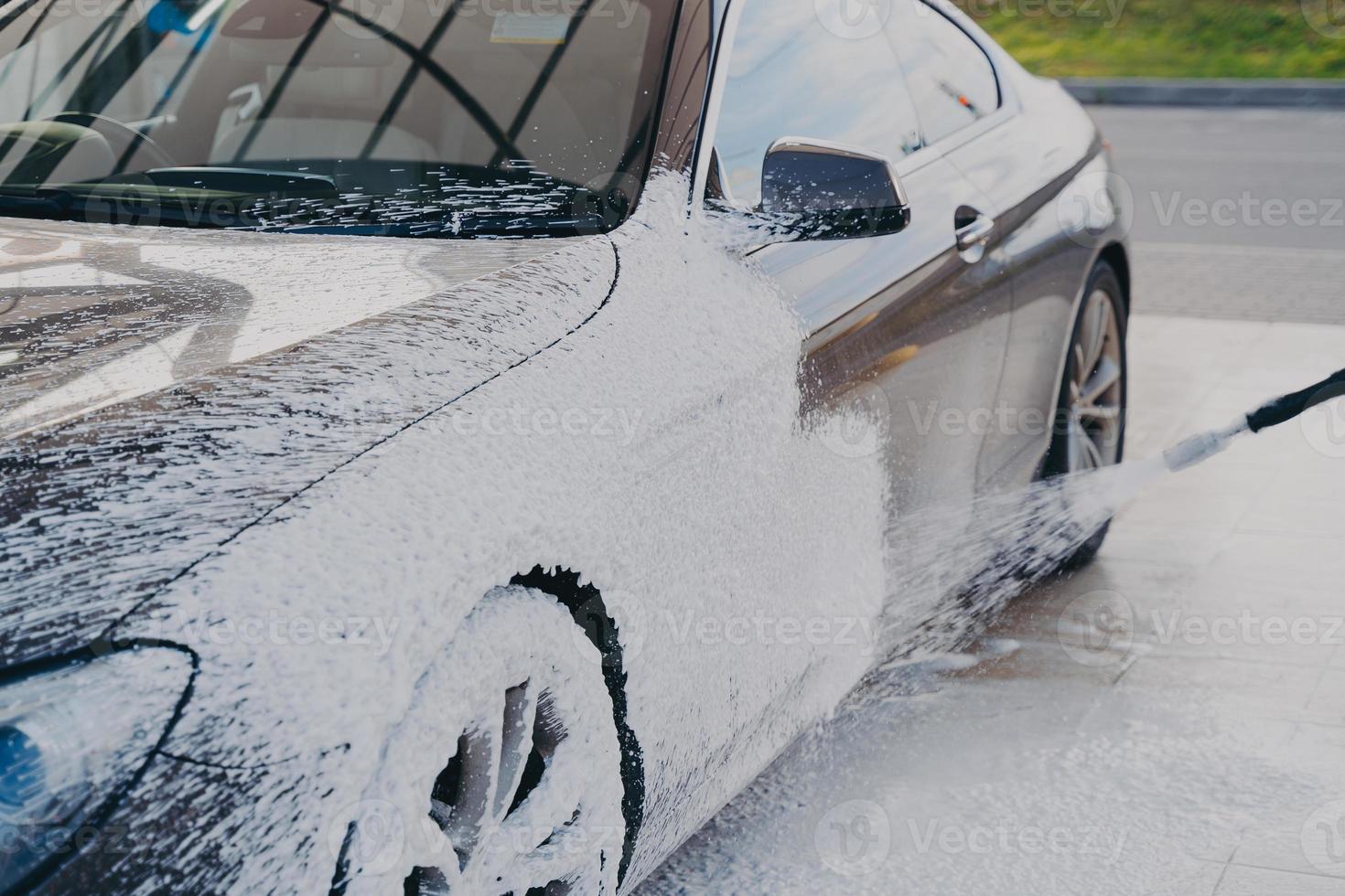 zwarte vuile auto in wit zeepschuim bij carwash-servicestation foto