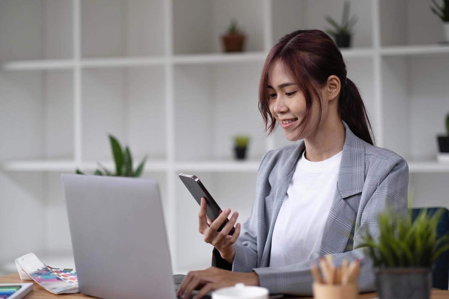 Aziatische vrouw ontwerper werkt met behulp van een smartphone leeg wit computerscherm aan tafel geplaatst met kleurstalen foto