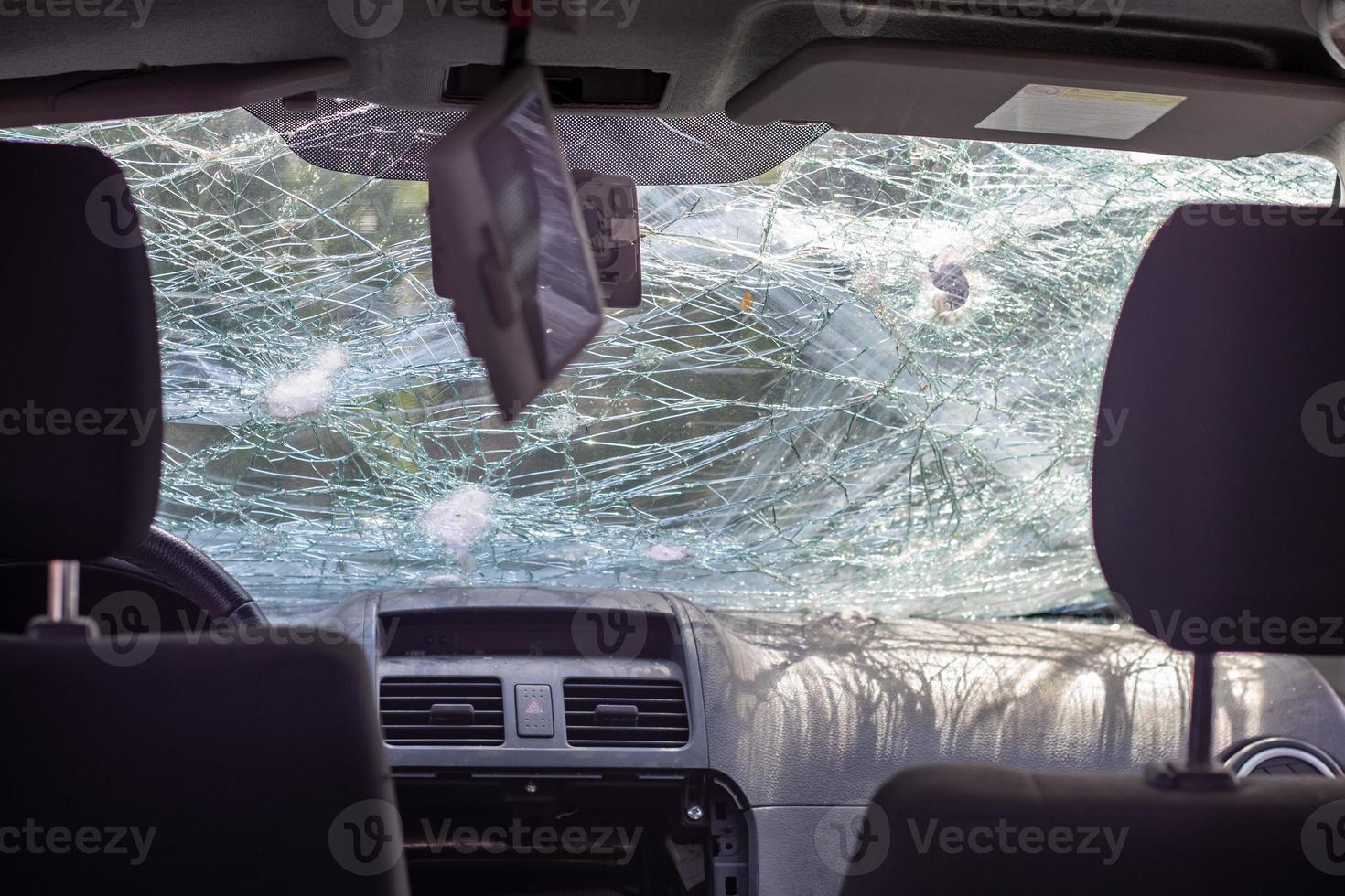 gebroken voorruit van een auto door een kogel, van een schot van een vuurwapen, zicht vanuit de binnenkant van de cabine. beschadigd glas met sporen van een naderende steen op de weg. binnenaanzicht van de auto. foto