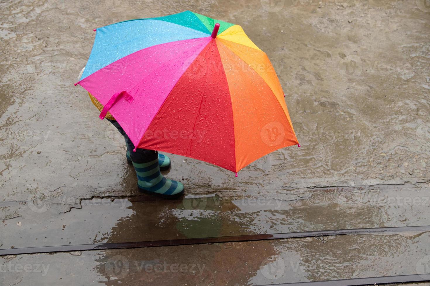 een 3-jarig meisje verstopt zich in de regen onder een gekleurde paraplu foto