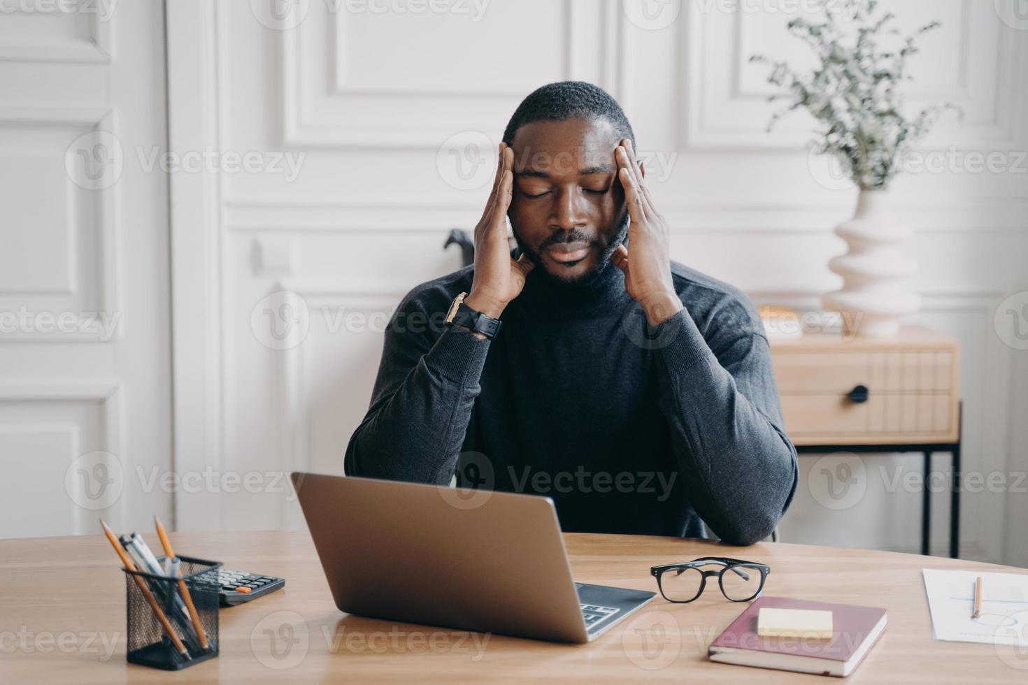 bezorgde jonge Afro-Amerikaanse man werknemer die lijdt aan hoofdpijn op de werkplek foto