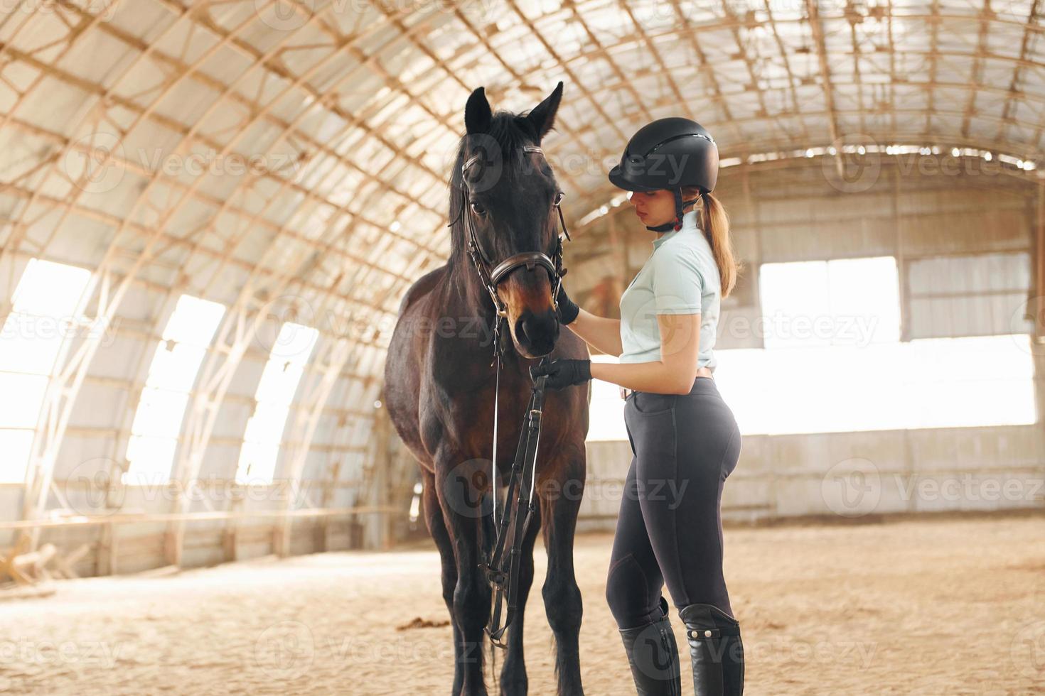 in beschermende hoed. een jonge vrouw in jockeykleding bereidt zich voor op een ritje met een paard op een stal foto