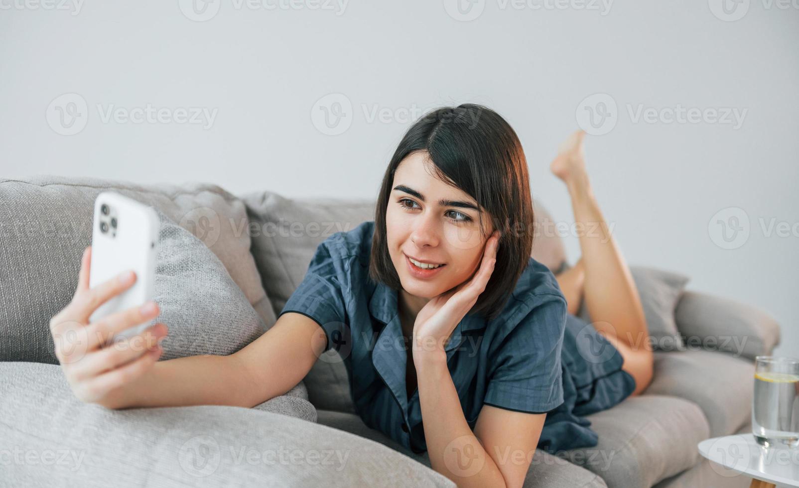 met telefoon. op de bank gaan liggen. jonge vrouw is thuis. conceptie van schoonheid foto