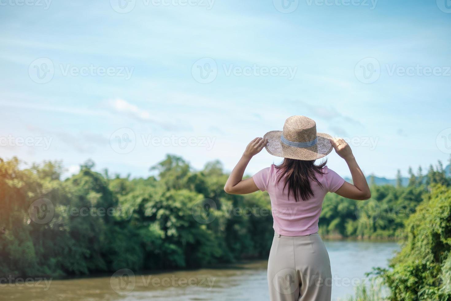 solo vrouw in roze en hoed reizen in de buurt van rivier. gelukkig meisje in de natuur. populair voor toeristenattracties in kanchanaburi, thailand foto