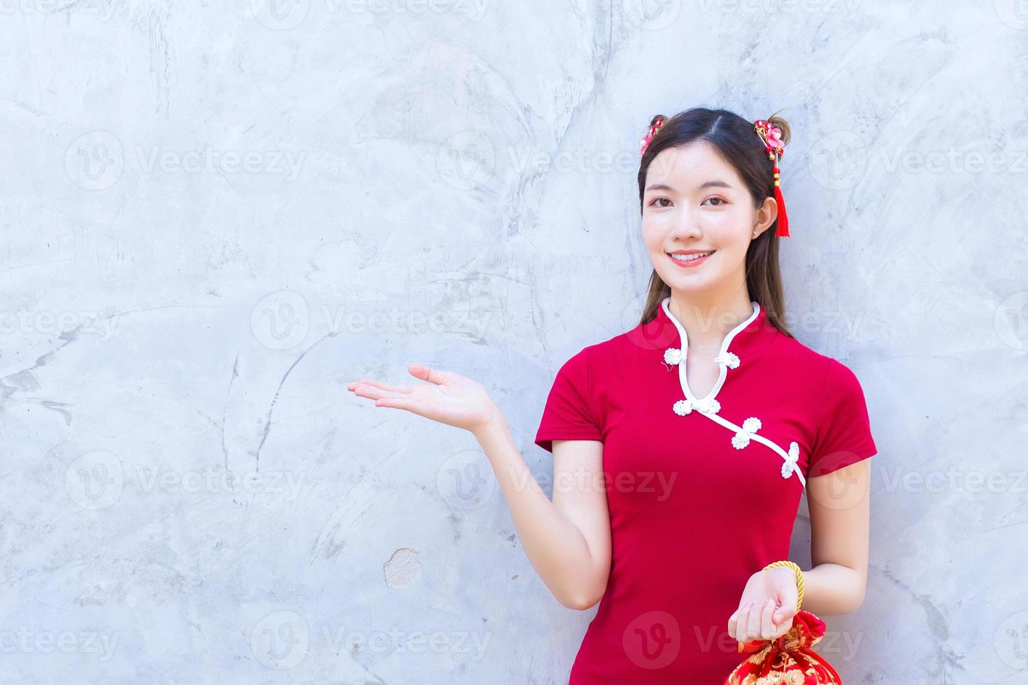 Aziatische mooie vrouw in rode jurk staat om iets op de grijze achtergrond te presenteren. Chinees nieuwjaarsthema. foto