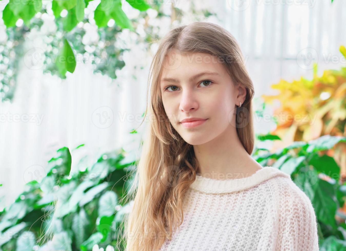 portret van een tienermeisje in haar huis in huis tuinkamer. groene planten op een achtergrond. rustige zelfverzekerde tiener die naar de camera kijkt foto