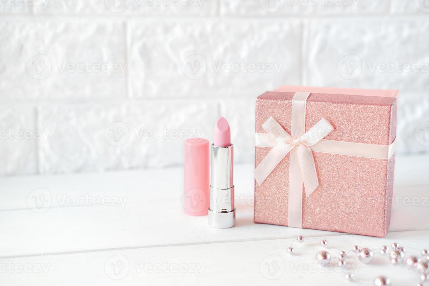 roze lippenstift en een geschenkdoos op een tafel. roze ketting. foto