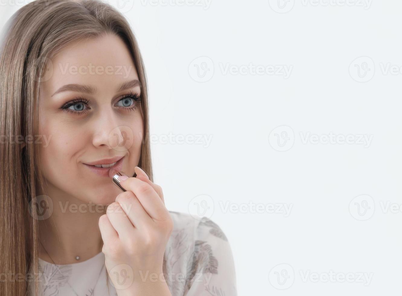 jonge vrouw die lippenstift aanbrengt en naar de spiegel kijkt. kaukasische vrouw met lang haar die zich klaarmaakt om uit te gaan. hydraterende lipverzorging..kopieer de ruimte foto