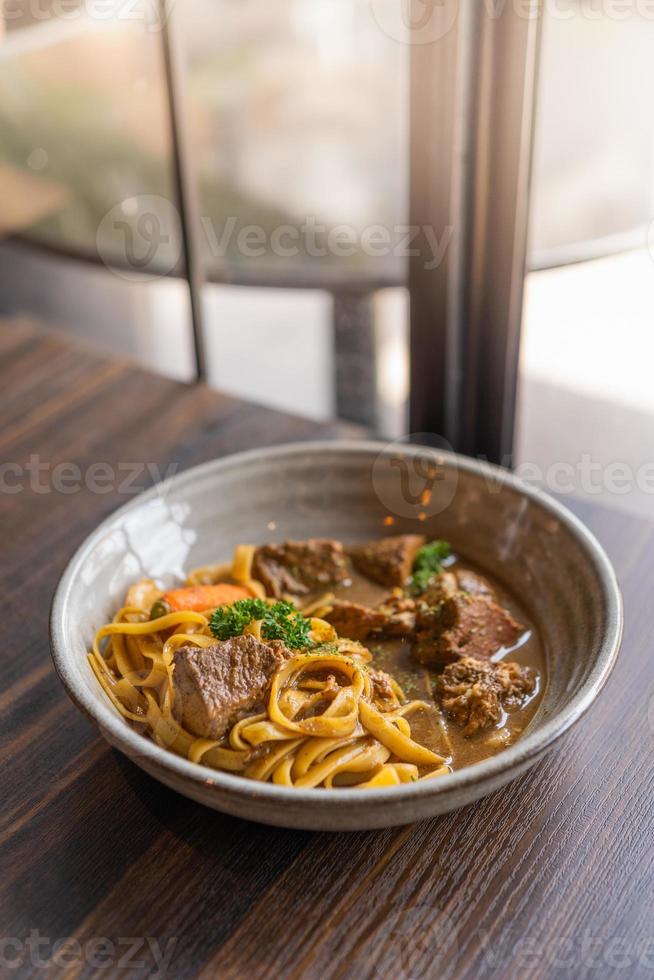 tagliatelle met varkensstoofpot en groenten in een kom geserveerd op houten tafel foto