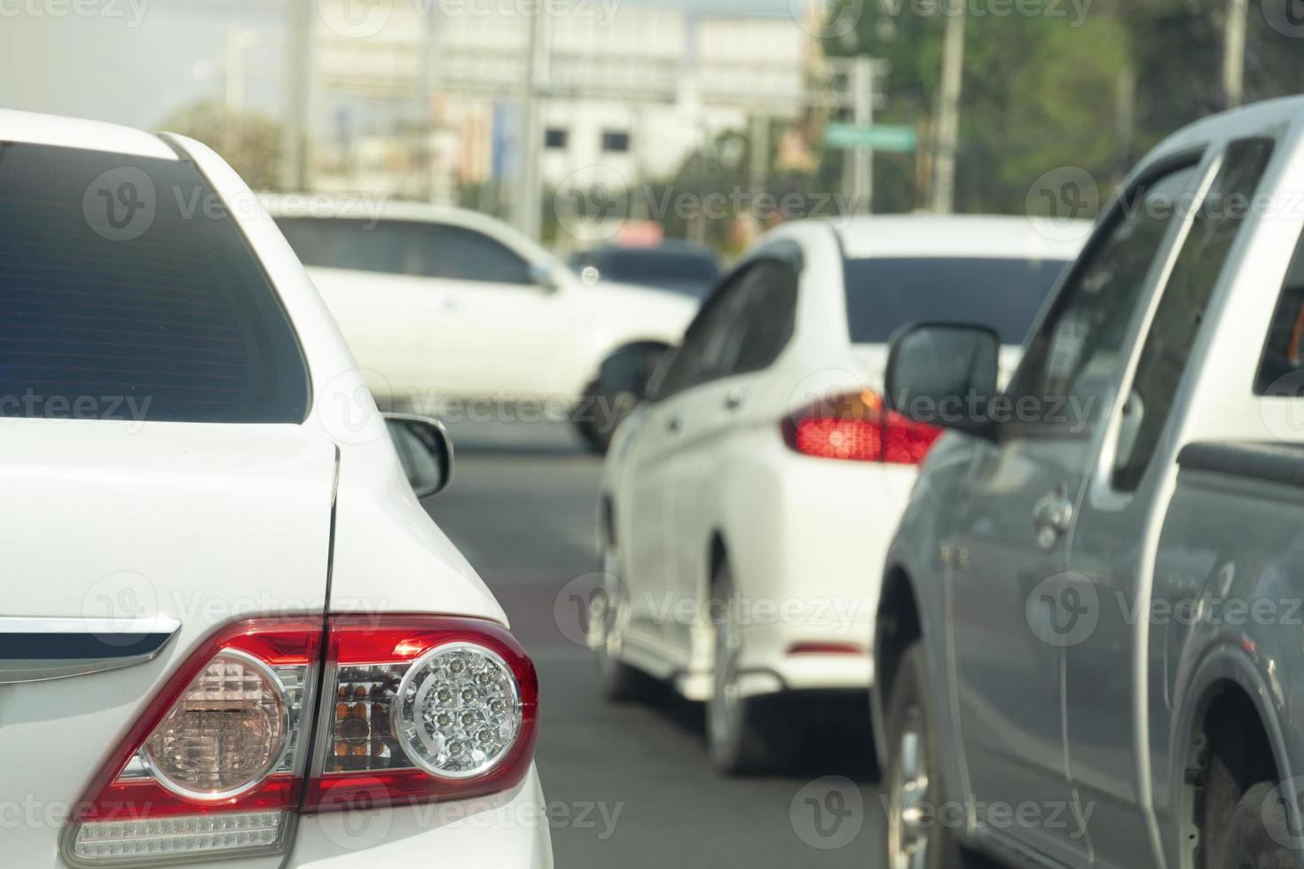 achterkant van witte auto rijden of stoppen op de asfaltweg. met andere auto's ernaast. wazig van auto's rijden door de voorkant van de kruising in de stad. foto