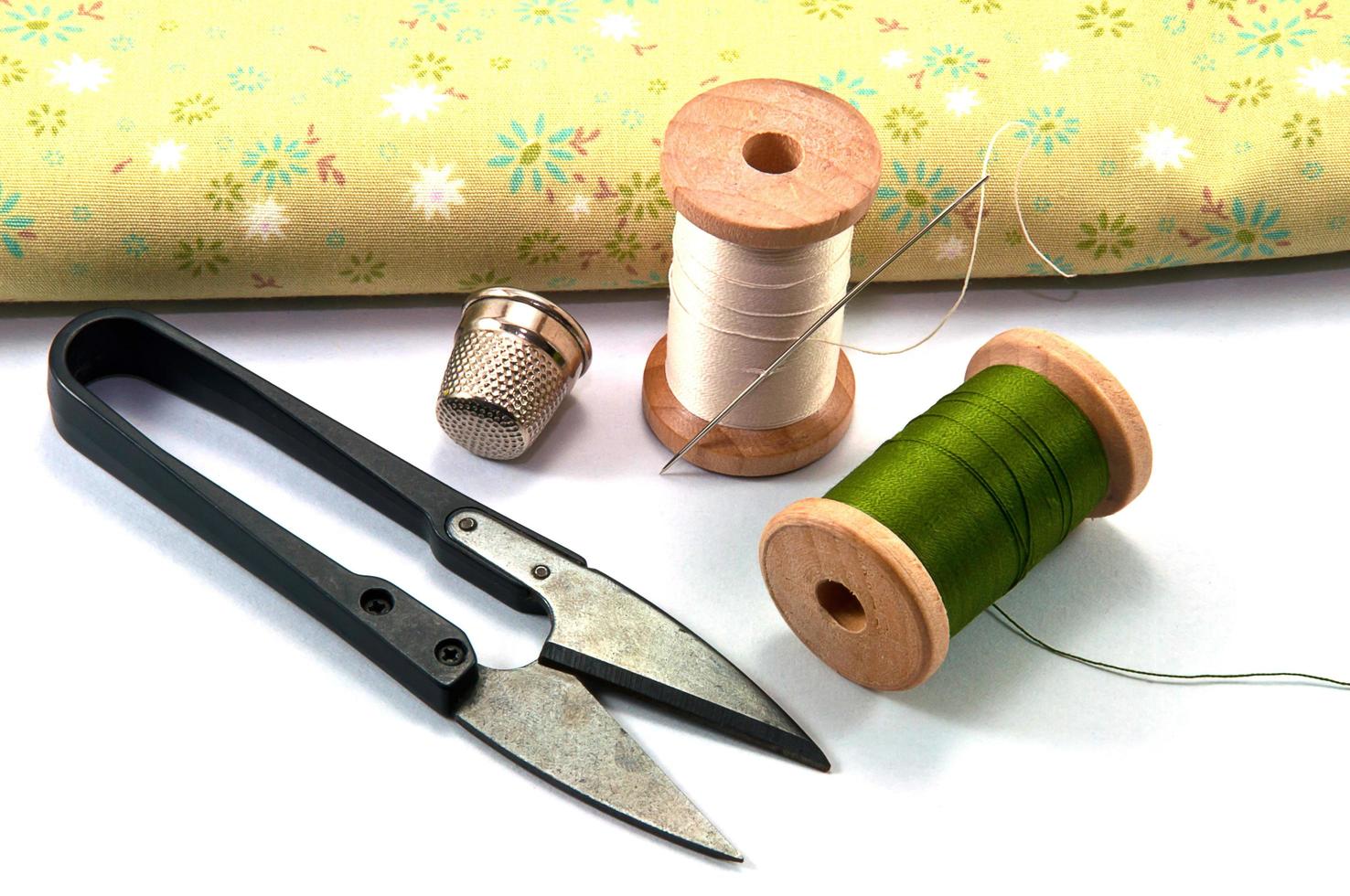 vingerhoed, naald, spoelen en schaar met doek voor het naaien op witte achtergrond foto