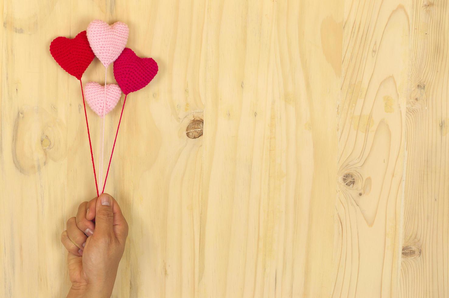 hand met drijvend rood en roze gehaakt hart over houten achtergrond foto