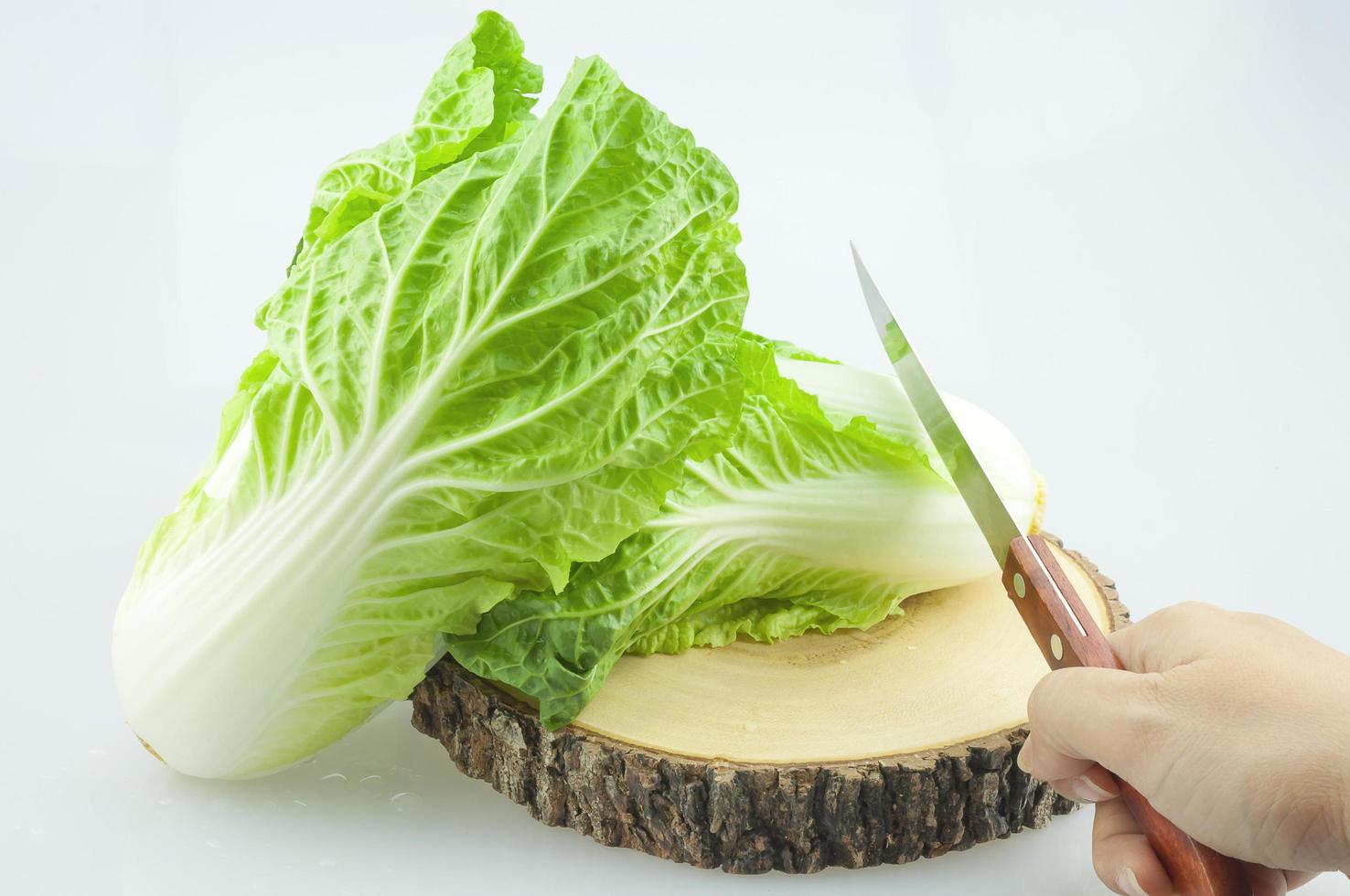 chinese kool op hakblok wordt gesneden door een keukenmes in de hand op een witte achtergrond. foto