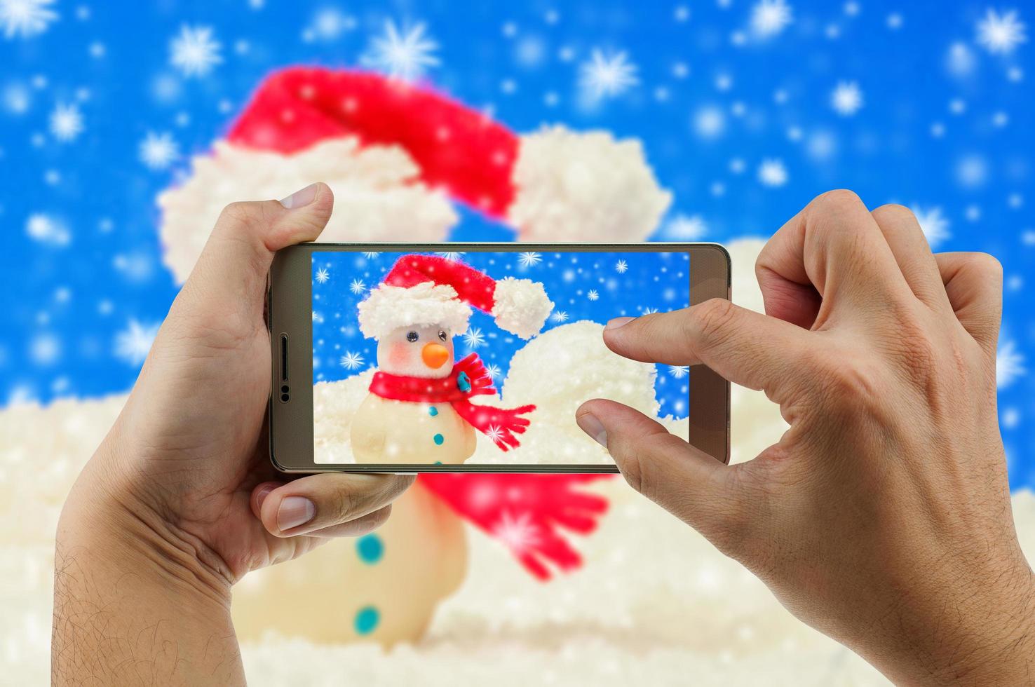 man die mobiele telefoon gebruikt om zoomfoto van sneeuwpop met onscherpe achtergrond te bekijken. kerstmis vieren gelukkig nieuwjaar festival foto