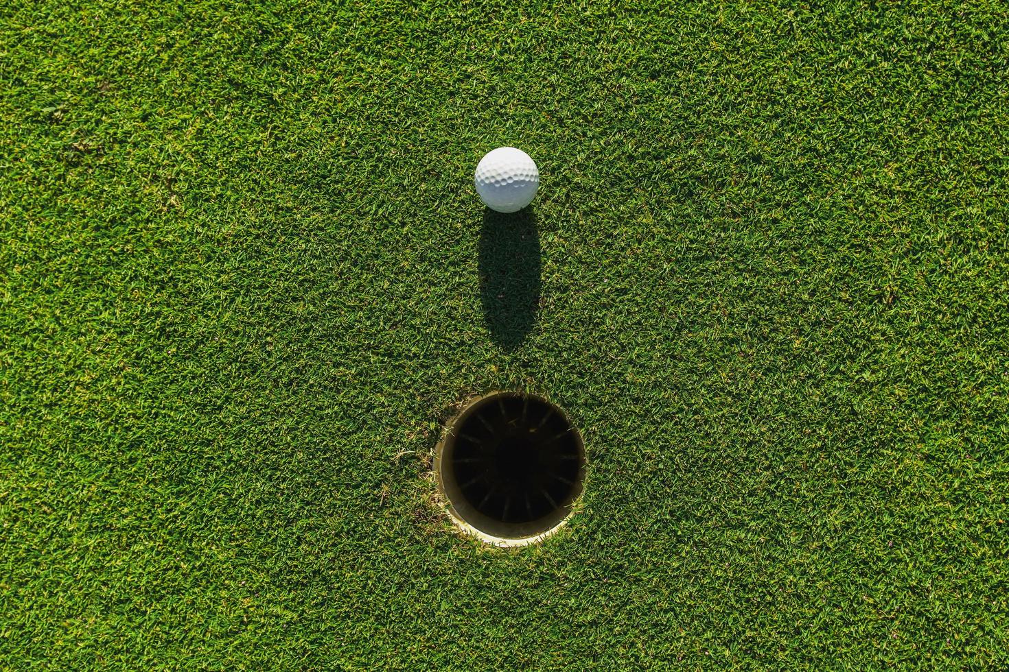 golfbal op groen gras met gat en zonlicht foto