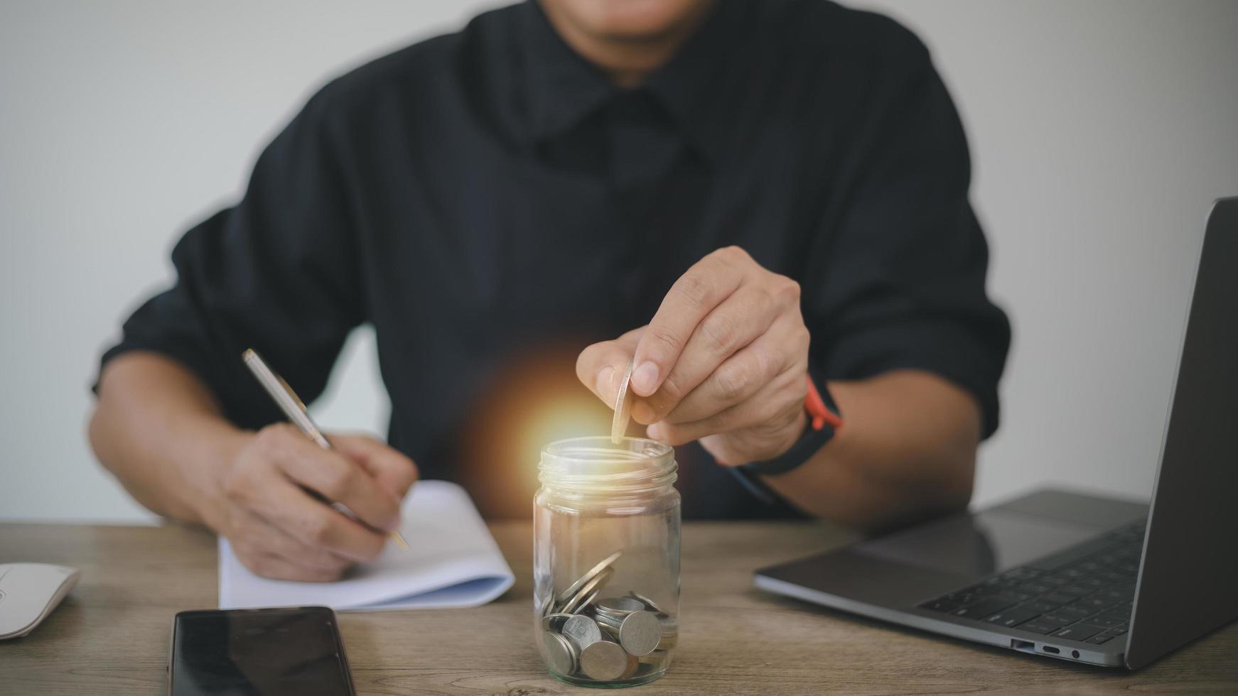 man hand munten in glazen fles bank zetten voor rekening geld besparen. planning opvoeren, geld sparen voor toekomstig plan, pensioenfonds. een boekhoudconcept voor bedrijfsinvesteringen en financiën foto