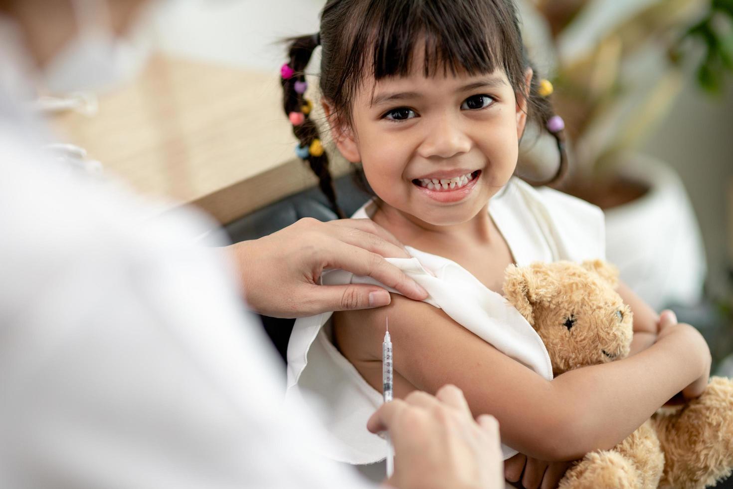 vaccinatie concept. vrouwelijke arts die schattig klein meisje in kliniek vaccineert foto