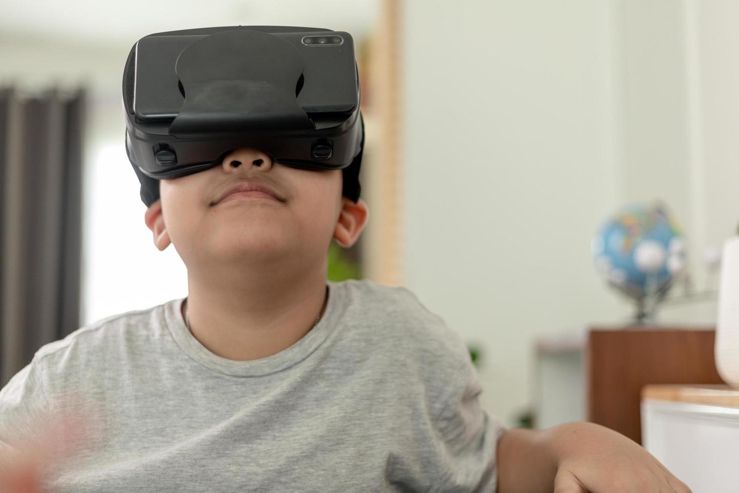 Aziatische kleine jongen met vr-bril die thuis wetenschappen studeert, nieuwsgierige student draagt een virtual reality-headset om wetenschap thuis online te studeren, futuristische levensstijl te leren foto