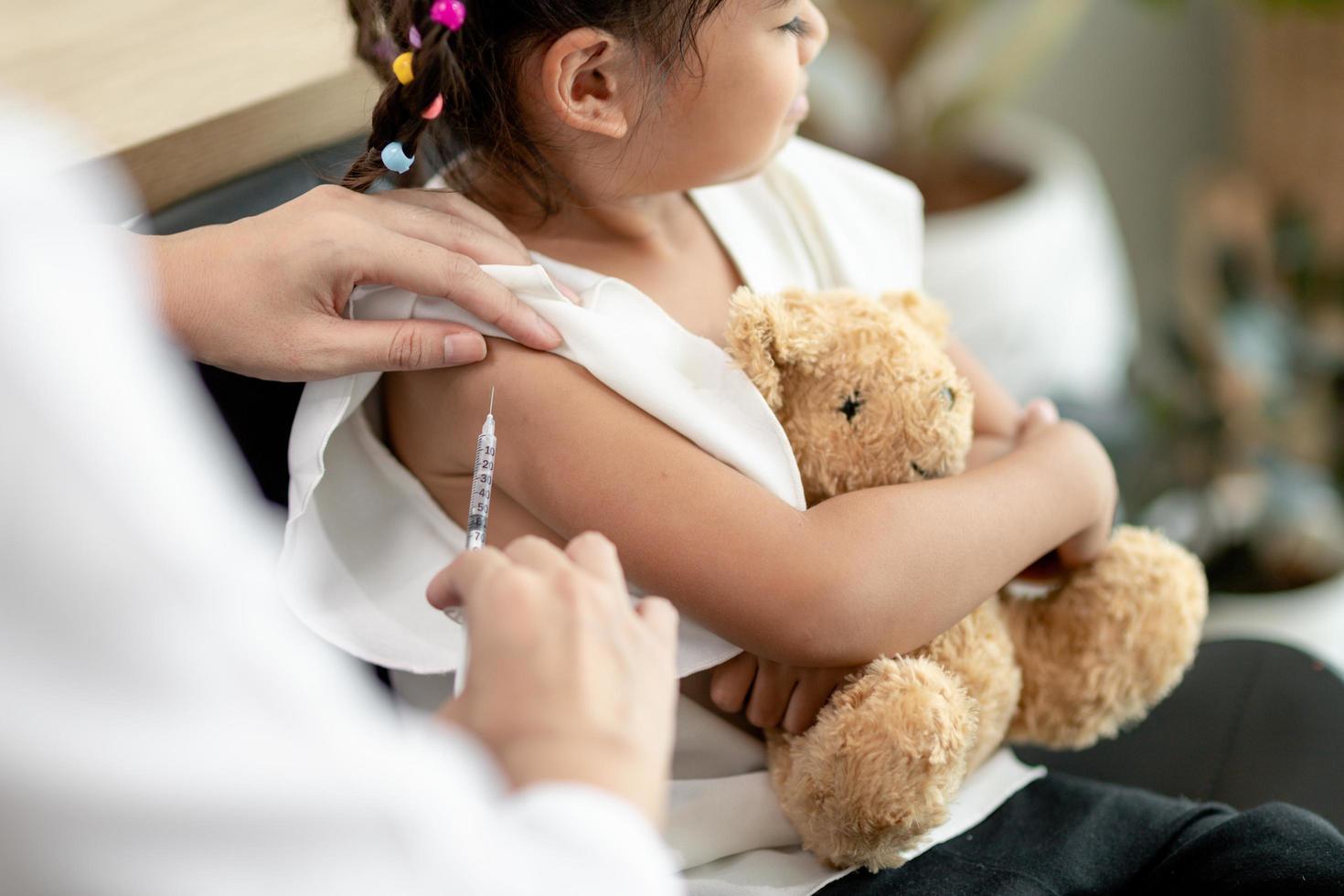 vaccinatie concept. vrouwelijke arts die schattig klein meisje in kliniek vaccineert foto