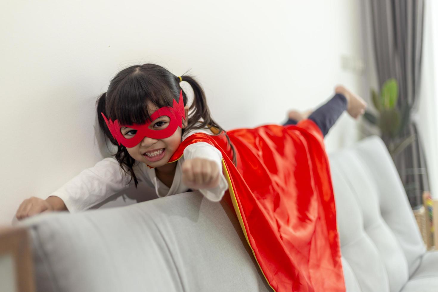 kindmeisje in een superheldenkostuum met masker en rode mantel thuis foto