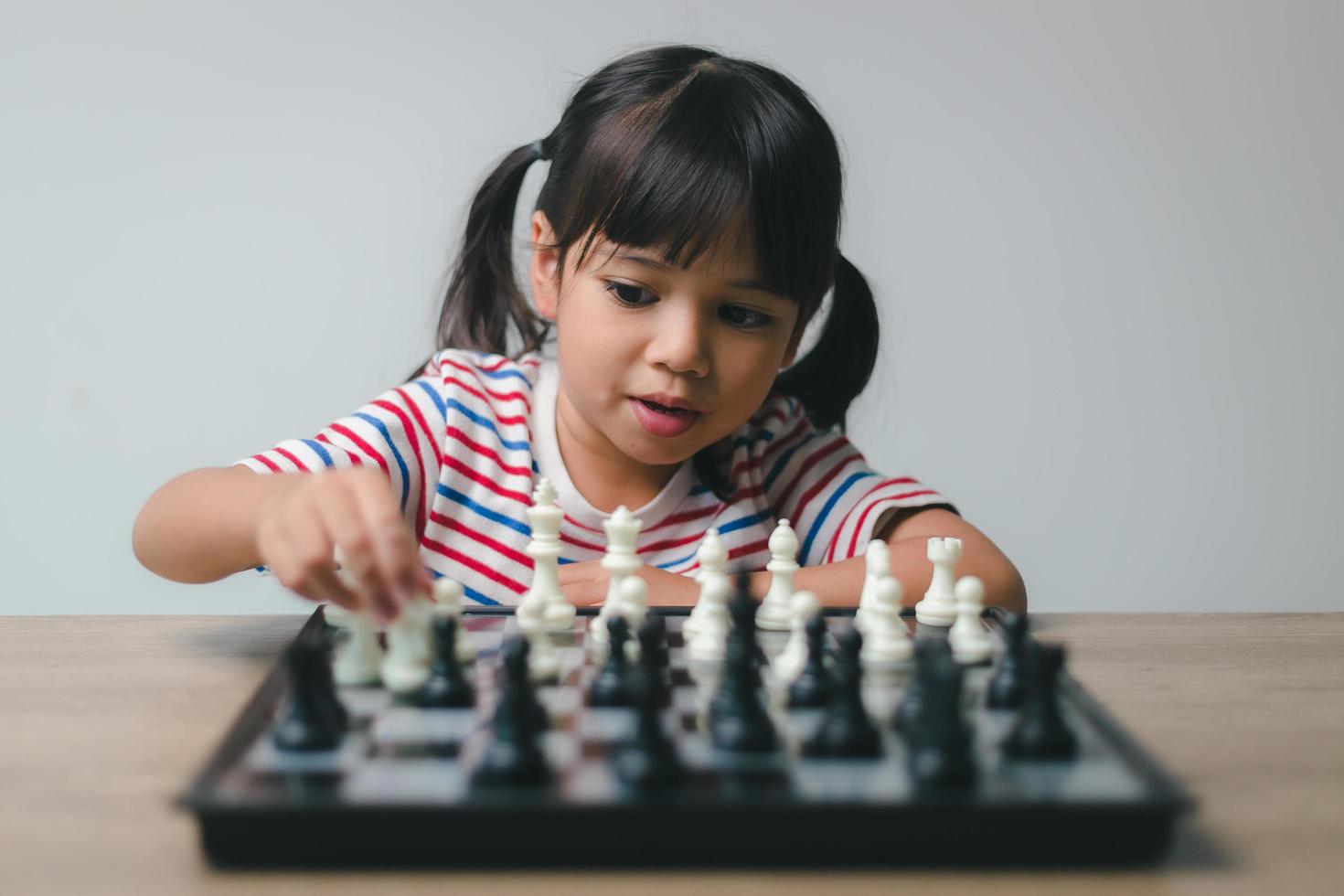 Aziatisch klein meisje schaakt thuis. Een spelletje schaak foto