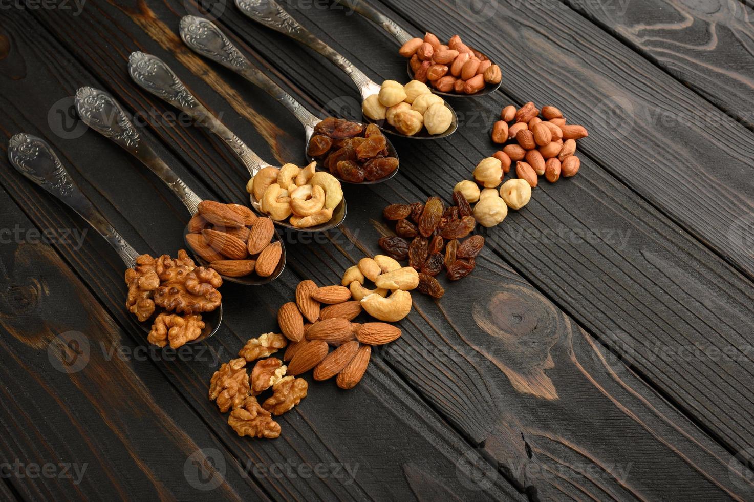 hazelnoot, cashewnoten, rozijnen, amandelen, pinda's, walnoten in zilveren lepels op een rustieke achtergrond foto