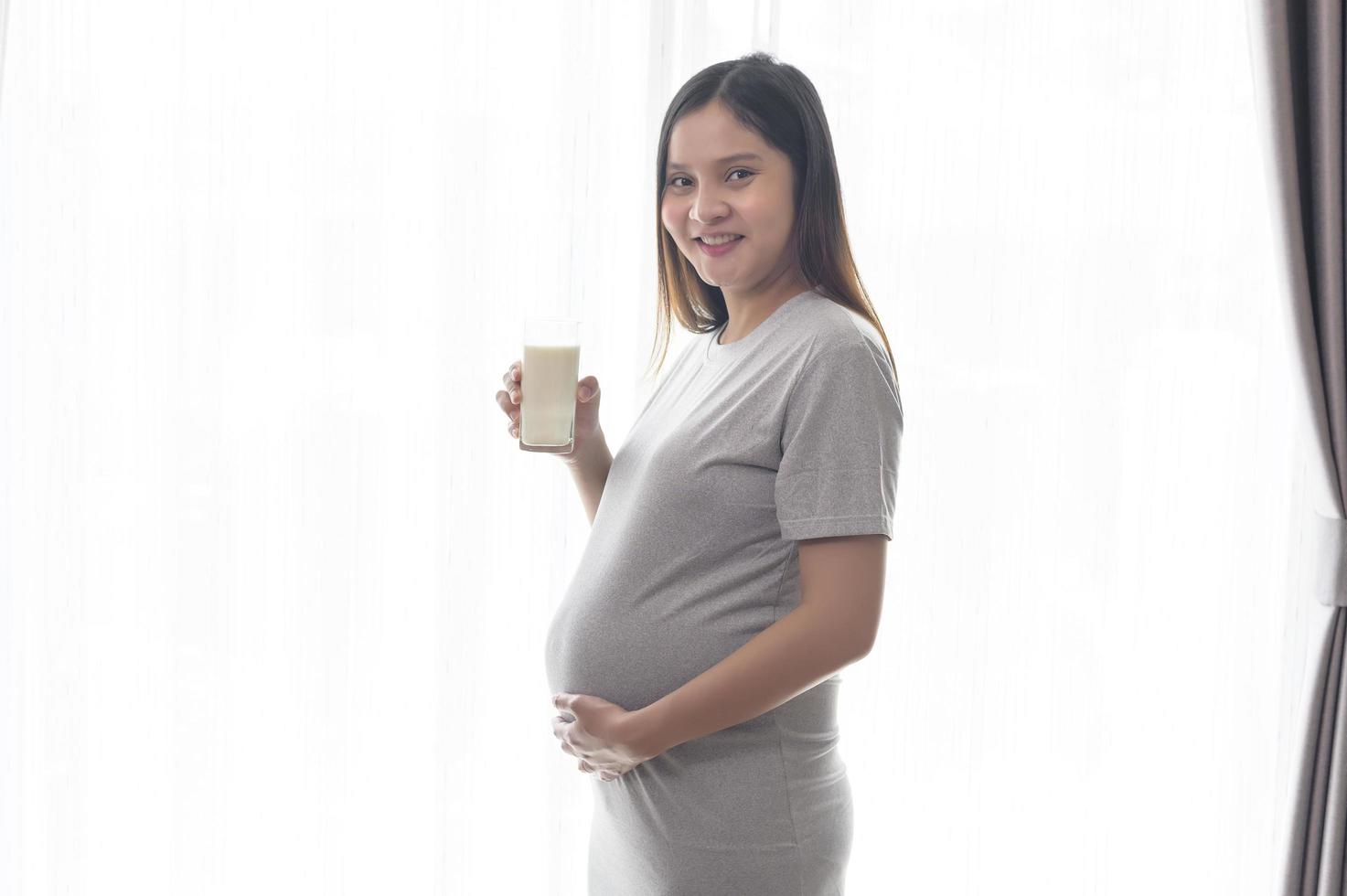 jonge zwangere vrouw die thuis melk drinkt, gezondheidszorg en zwangerschapszorg foto