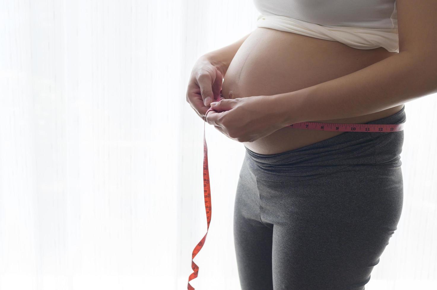 jonge zwangere vrouw die buikcentimeter meet, gezondheidszorg en zwangerschapszorg foto