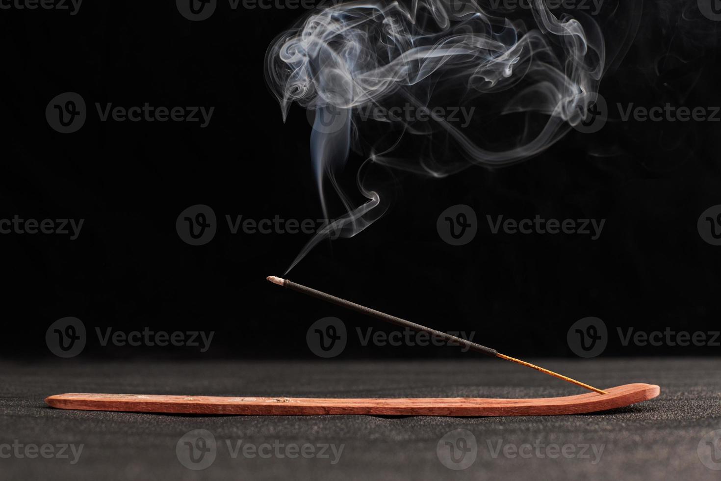 rook krullen van brandende wierookstokjes in houten houder voor ontspanning en meditatie zwarte achtergrond foto