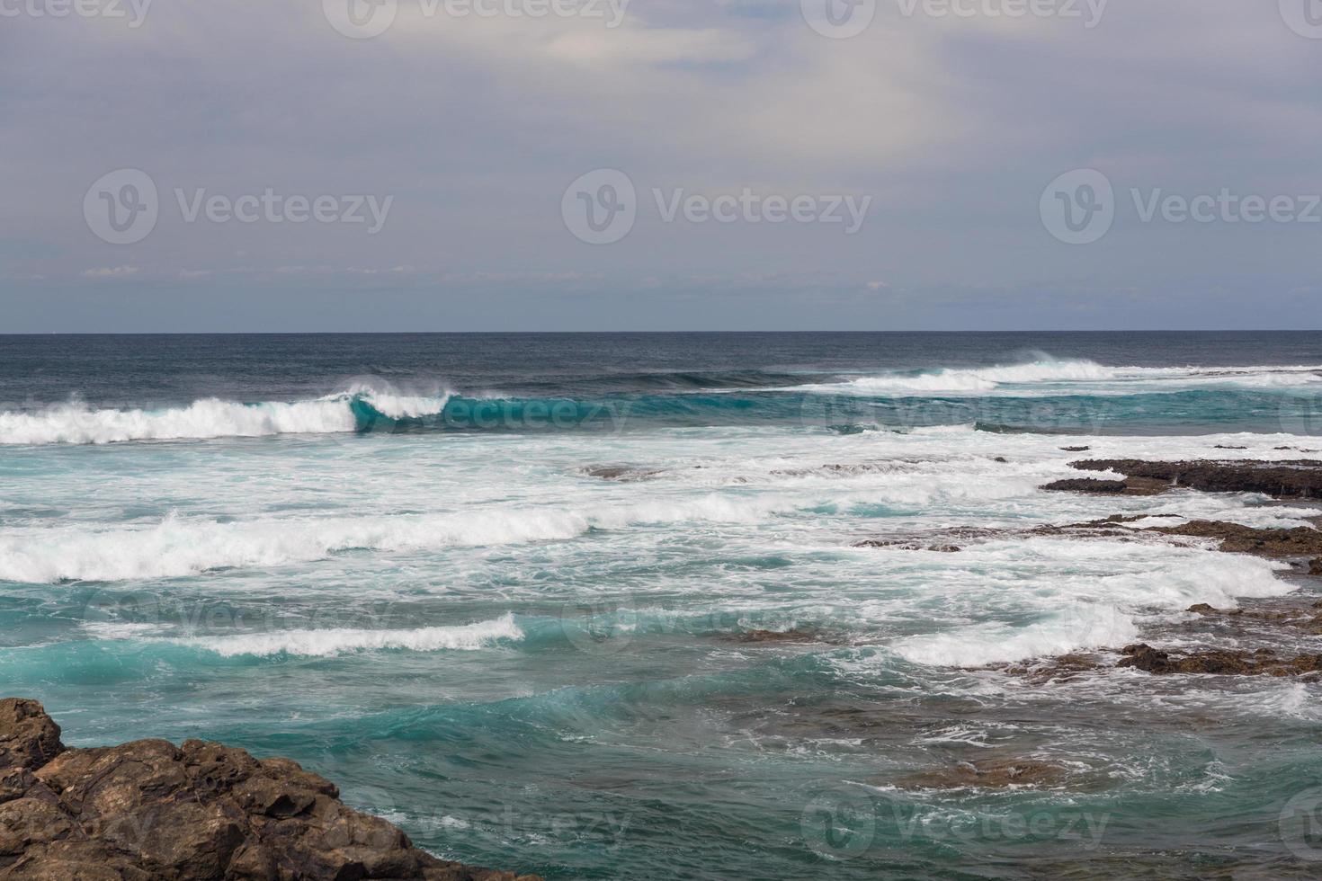 turbulente oceaangolven met wit schuim slaan kuststenen foto