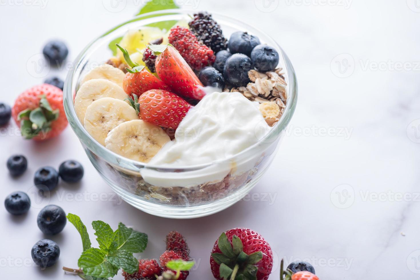 kom havergranola met yoghurt, verse bosbessen, moerbei, aardbeien, kiwi, banaan, munt en notenbord voor gezond ontbijt, bovenaanzicht, kopieerruimte, plat leggen. vegetarisch voedselconcept. foto