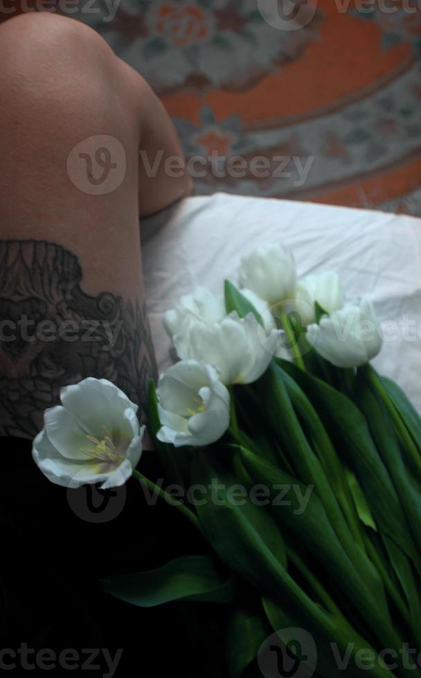 witte tulpen. mooie witte tulpen liggen op een witte sprei, zwarte tatoeage op het been van het meisje foto