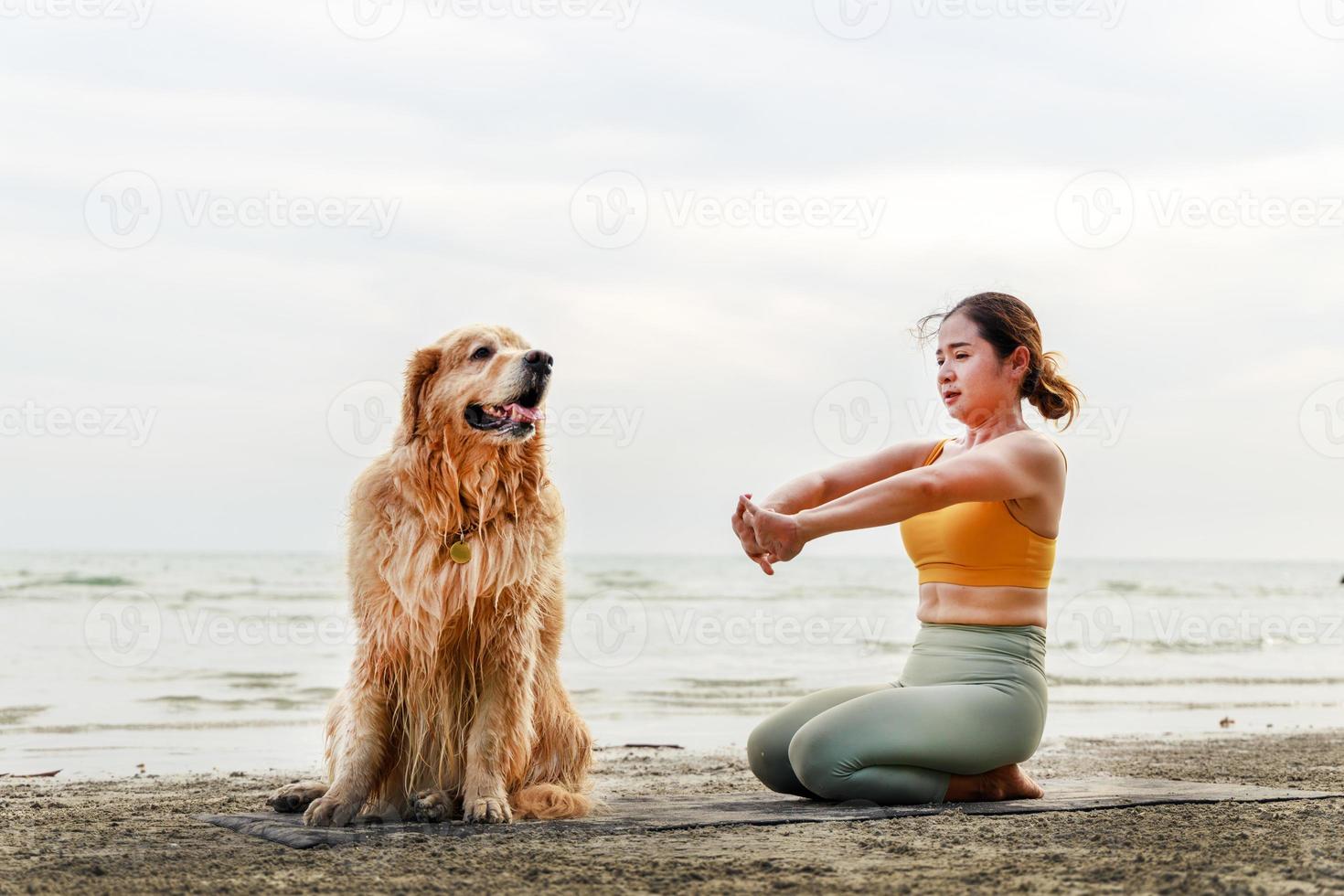 vrouw yoga-oefeningen op het strand met haar schattige hond. gezond actief levensstijlconcept. ontspanning met een huisdier. foto