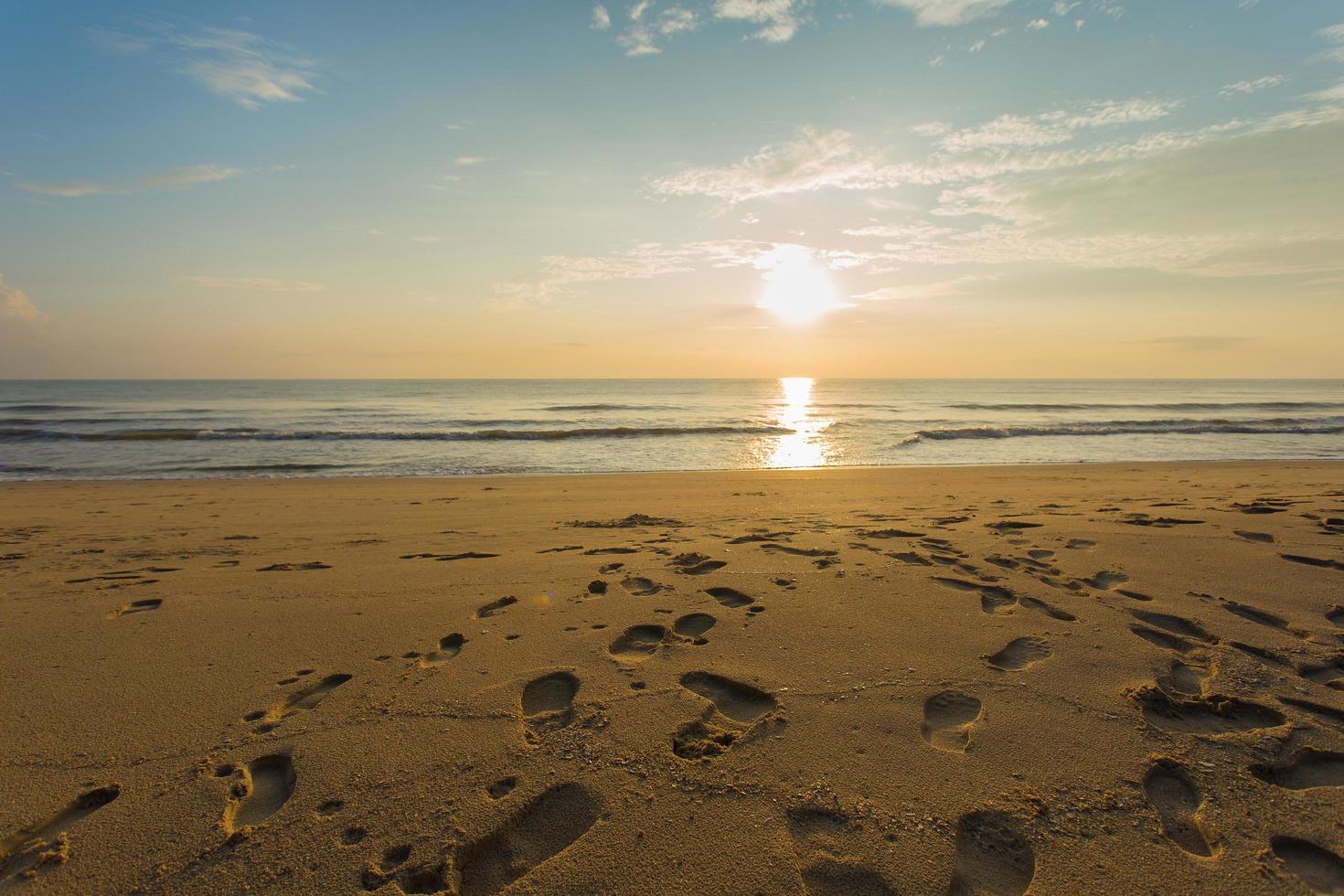 de voetafdrukken werden getoond op het zand in zee en zonsondergang met blauwe lucht. foto