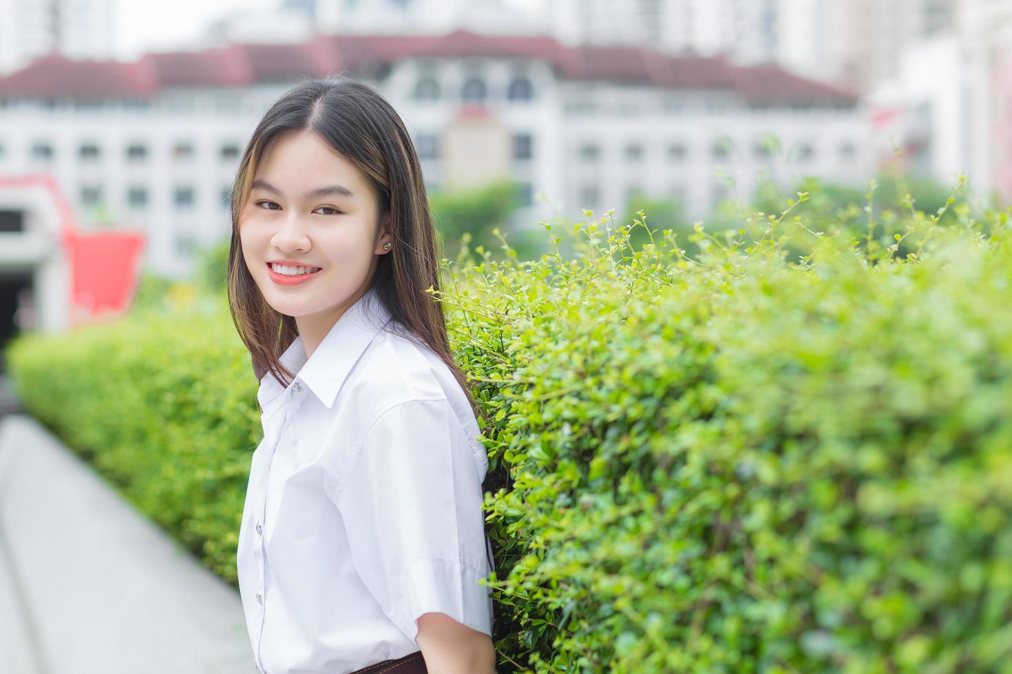 portret van volwassen Thaise student in uniform van de universiteitsstudent. Aziatische mooi meisje zit gelukkig lachend aan de universiteit in de buitenlucht met een achtergrond van bomen in de buitenlucht. foto