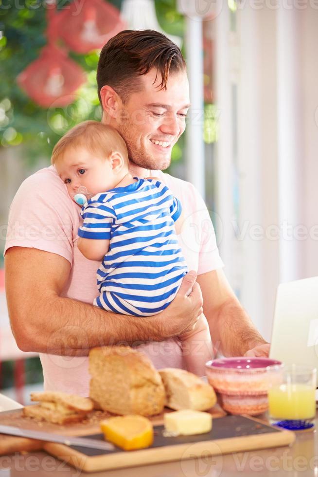 vader die baby houdt en snack maakt terwijl het gebruiken van laptop foto