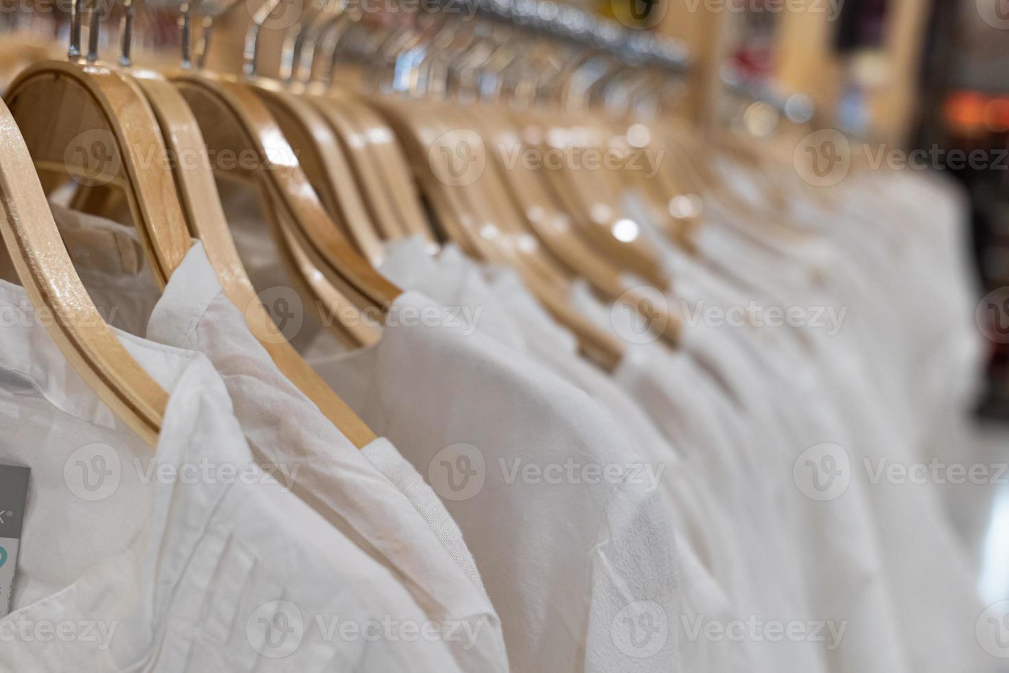 witte kleren die op houten rekken hangen. kleding voor vrouwen die aan hangers hangen in het winkelcentrum te koop. foto