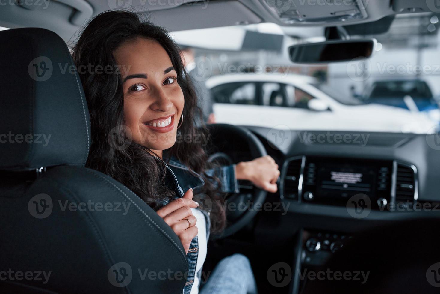 achteruit bewegen. ute meid met zwart haar probeert haar gloednieuwe dure auto in de autosalon foto
