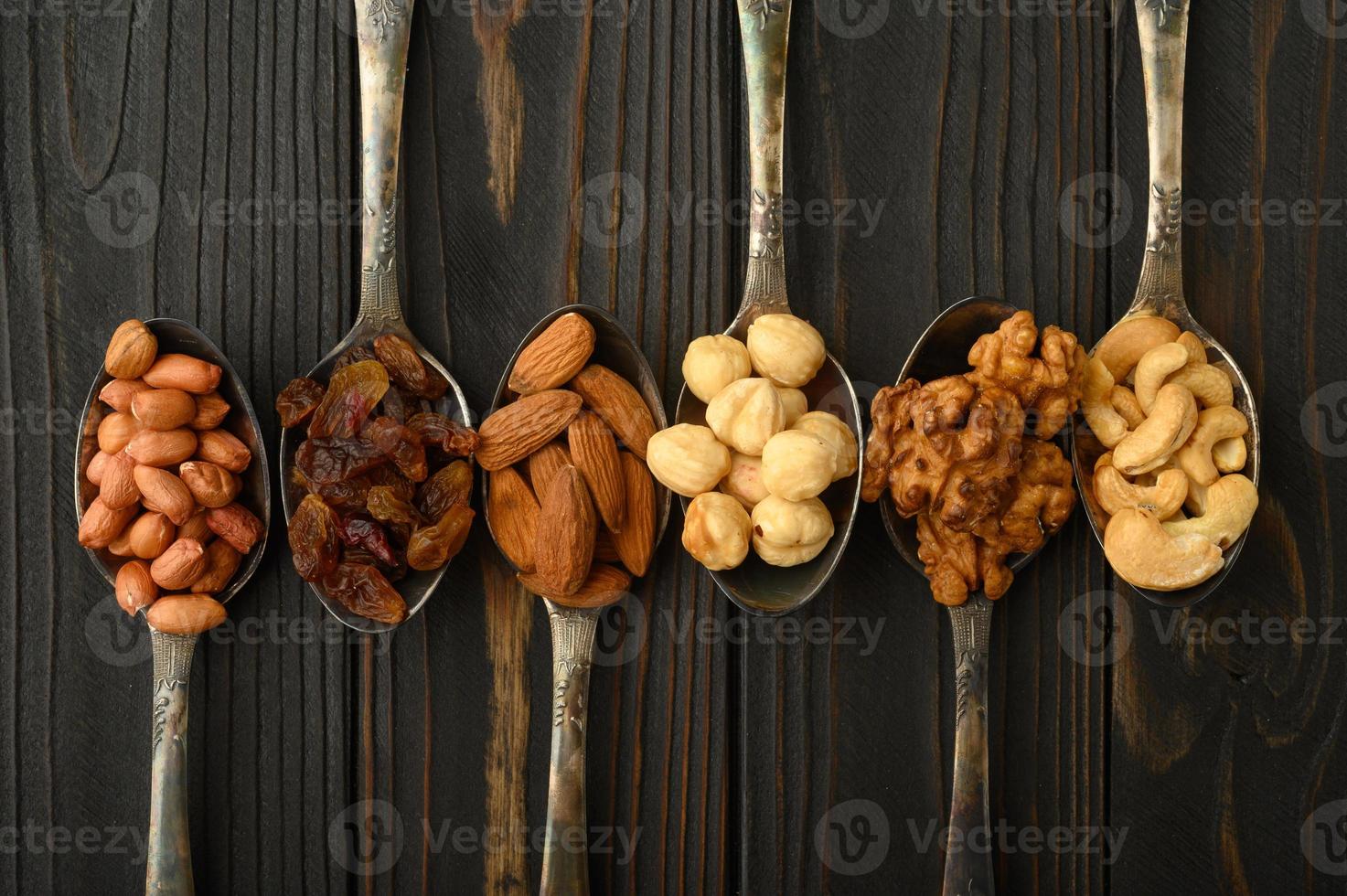 hazelnoot, cashewnoten, rozijnen, amandelen, pinda's, walnoten in zilveren lepels op een rustieke achtergrond foto