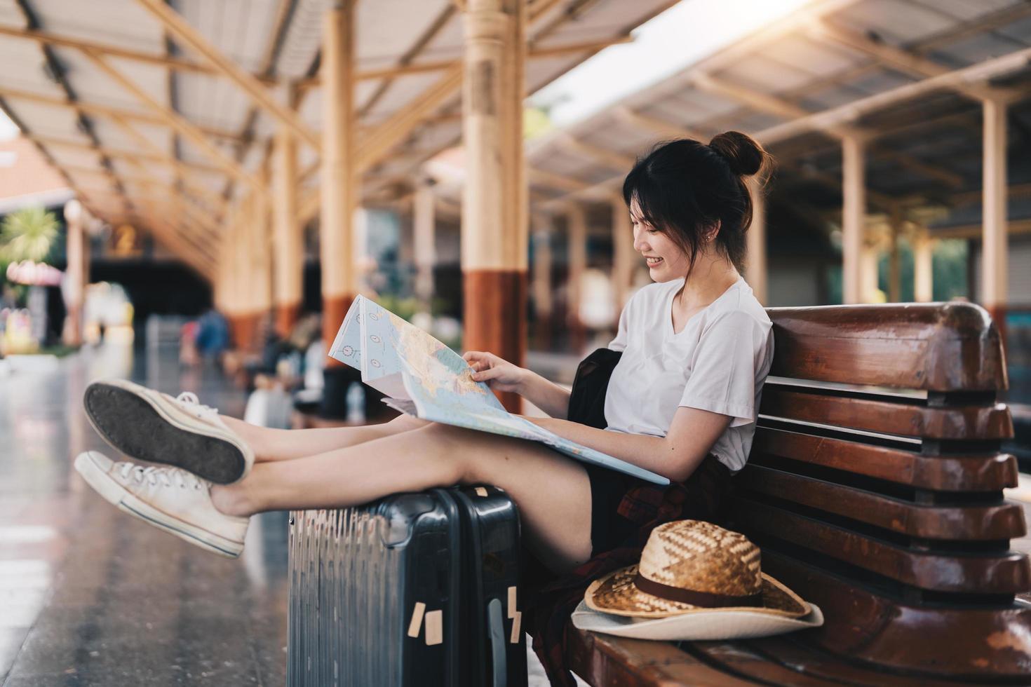 gelukkige jonge Aziatische vrouw reiziger of backpacker met behulp van kaart kiezen waar te reizen met bagage op treinstation, zomervakantie reisconcept foto