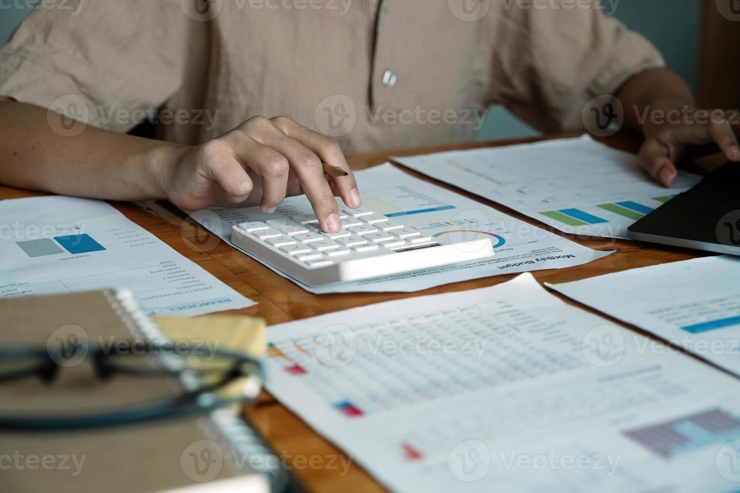 Close-up van zakenvrouw of accountant hand met pen bezig met rekenmachine om bedrijfsgegevens, boekhouddocument en laptopcomputer op kantoor, bedrijfsconcept te berekenen foto