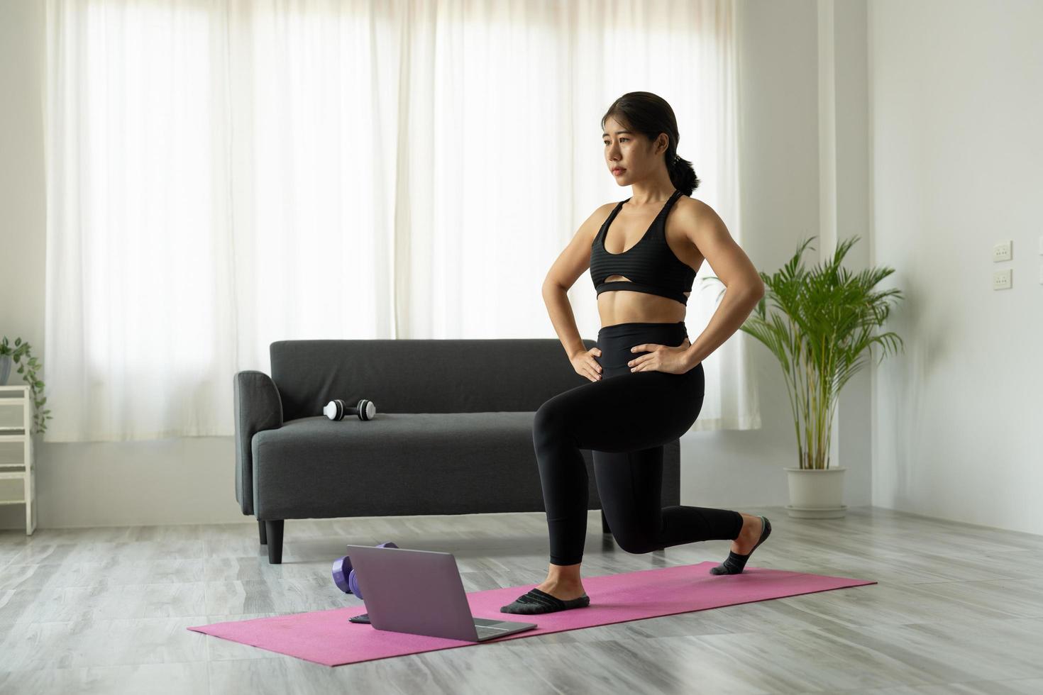 fit sportieve jonge aziatische vrouw online training oefening thuis. actieve gezonde meid geniet van sport pilates yoga fitness training op laptop computer die zich uitstrekt op yoga mat kijken naar video klasse foto