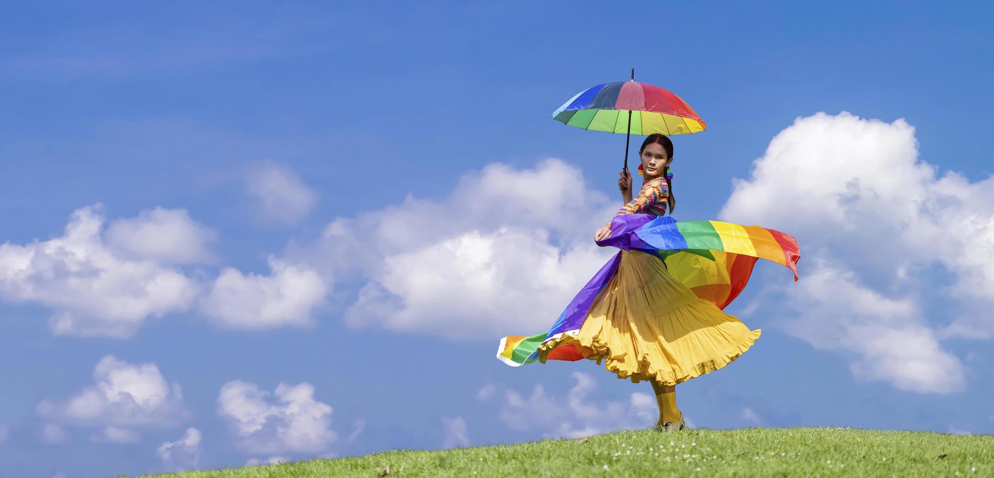 elegantie transgender vrouw in regenboogvlagkostuum en paraplu danst op de heuvel tijdens de zomer voor lgbtq pride-maand en komt uit de kast concept voor seksuele gelijkheid en vrijheid foto