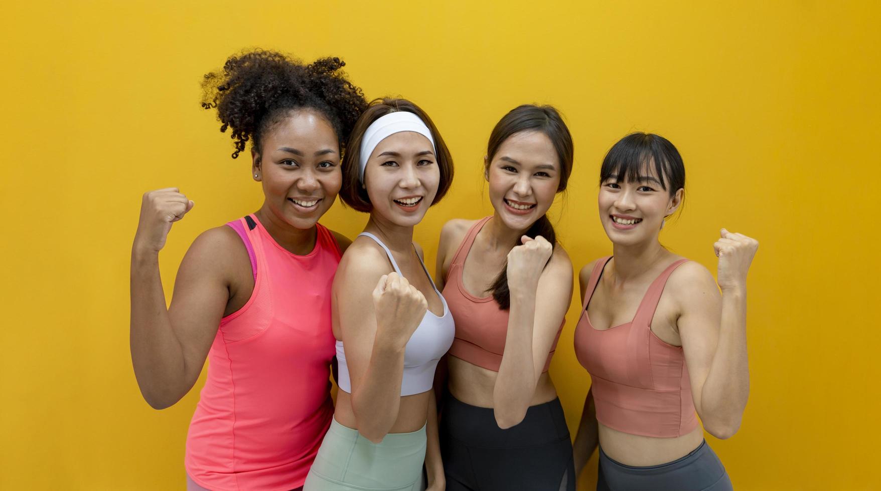 groepsportret van gezonde en slanke diversiteitsatletenvrouwen in sportkleding die op de geïsoleerde gele achtergrond glimlachen voor bewegings- en trainingsconcept foto