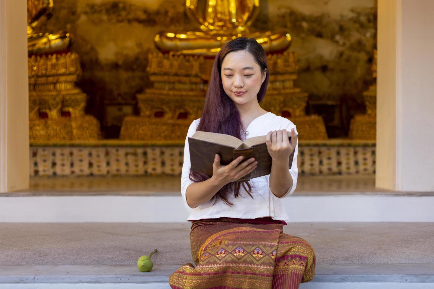 Aziatische boeddhistische vrouw leest Sanskriet oude tripitaka boek van heer Boeddha dhamma onderwijs terwijl ze in de tempel zit om te zingen en te aanbidden in het klooster foto