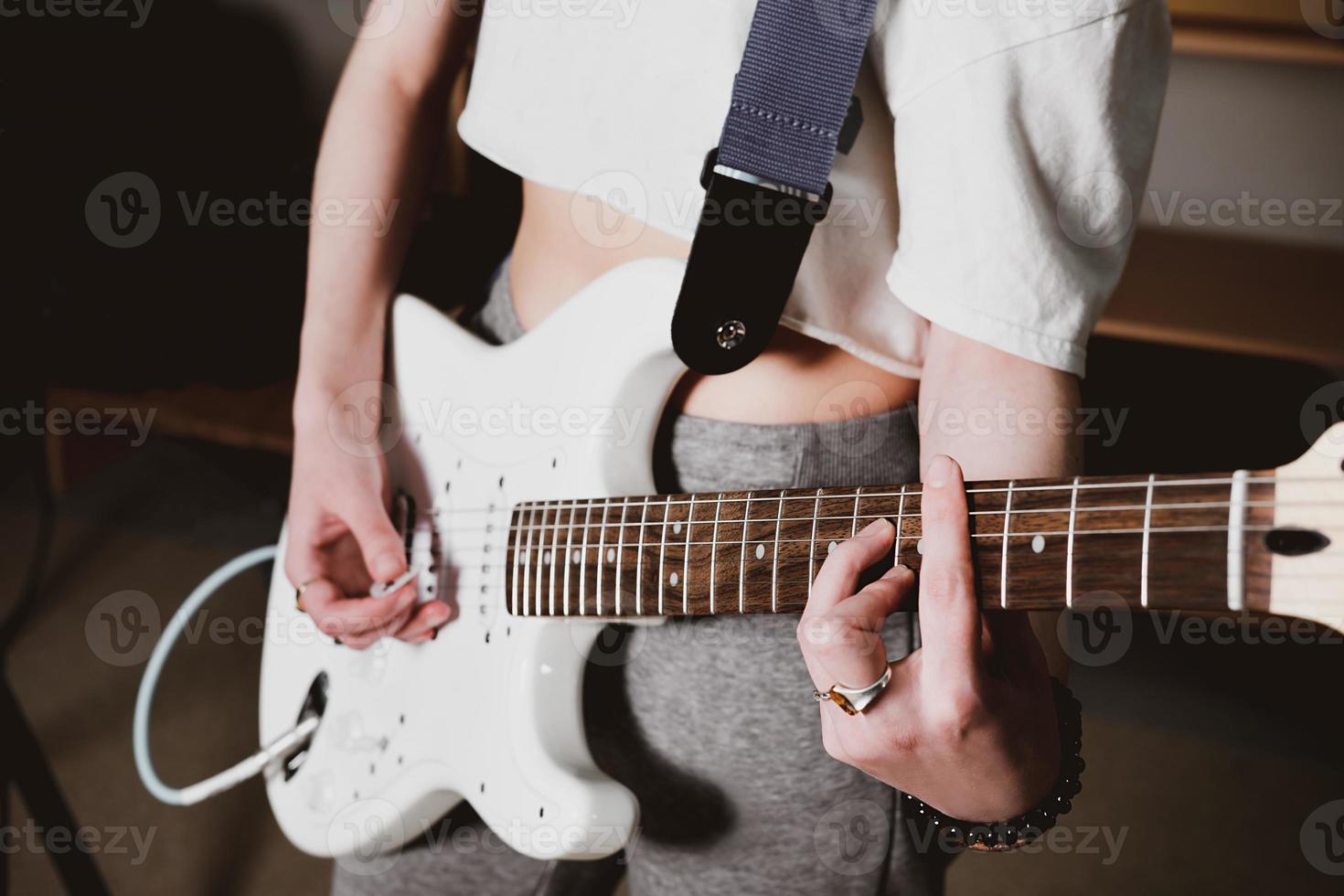 vrouwelijke artiest die elektrische gitaar speelt en een lied uitvoert. weergave bijsnijden. vrouw met witte gitaar die thuis repeteert. muziek als hobby en creatieve vrijetijdsbesteding. selectieve focus foto