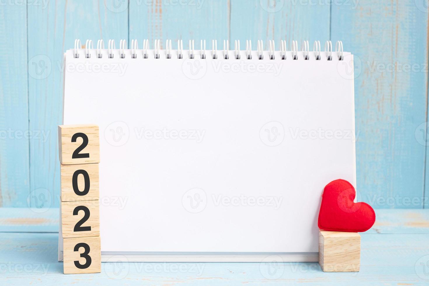 leeg notitieboekje en 2023 kubussen met rode hartvorm decoratie op blauwe houten tafel achtergrond. nieuwjaar newyou, doel, resolutie, gezondheid, liefde en happy valentine day concept foto