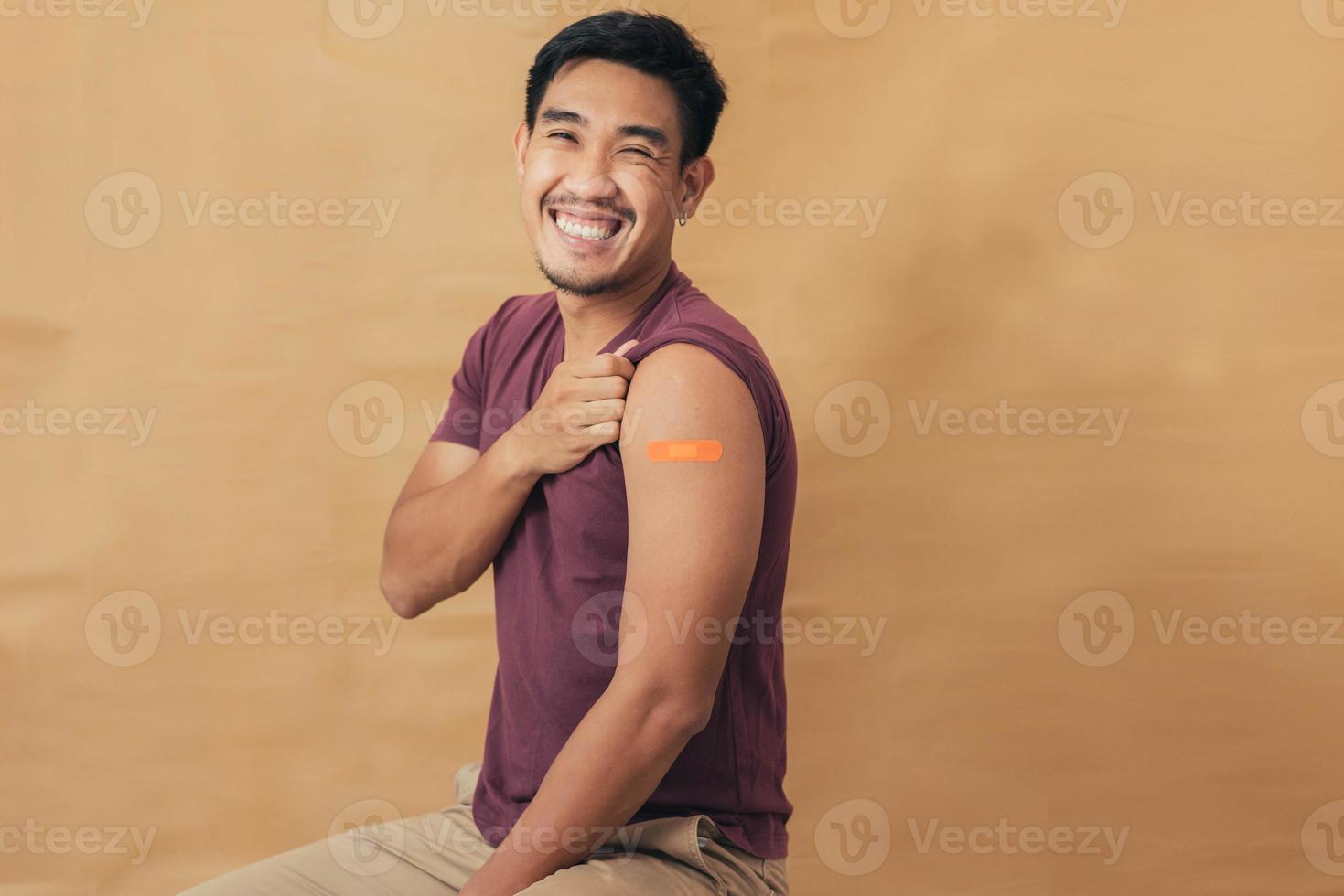 aziatische man die schouders toont na het krijgen van een vaccin. gelukkige man die arm toont met pleisters op na vaccininjectie. foto
